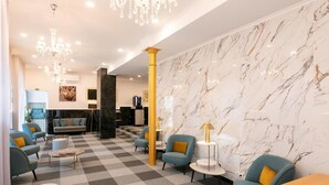 Un hall con suelo a cuadros, sillones azules, una araña de cristal, paredes de mármol y un mostrador de recepción.