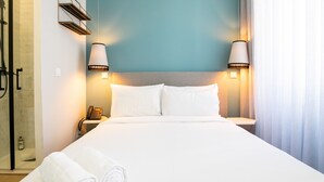 Habitación de hotel con cama, dos lámparas de noche, mesita con teléfono y zona de ducha.