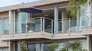 A modern building with a balcony featuring a glass railing, a table with chairs, and an umbrella.