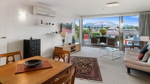 A modern living room with a dining area, a sofa, and a balcony with a view of mountains.