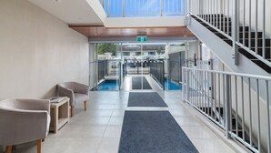 A modern hotel lobby with a glass entrance, a staircase, and seating area.