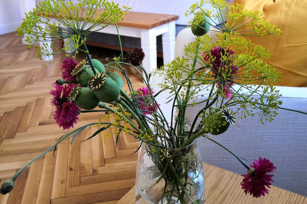 Een kamer met een bed, een nachtkastje en een vaas met bloemen op een houten vloer.