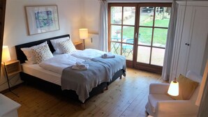 A bedroom with a bed, two bedside lamps, a chair, and a view of the outdoors.