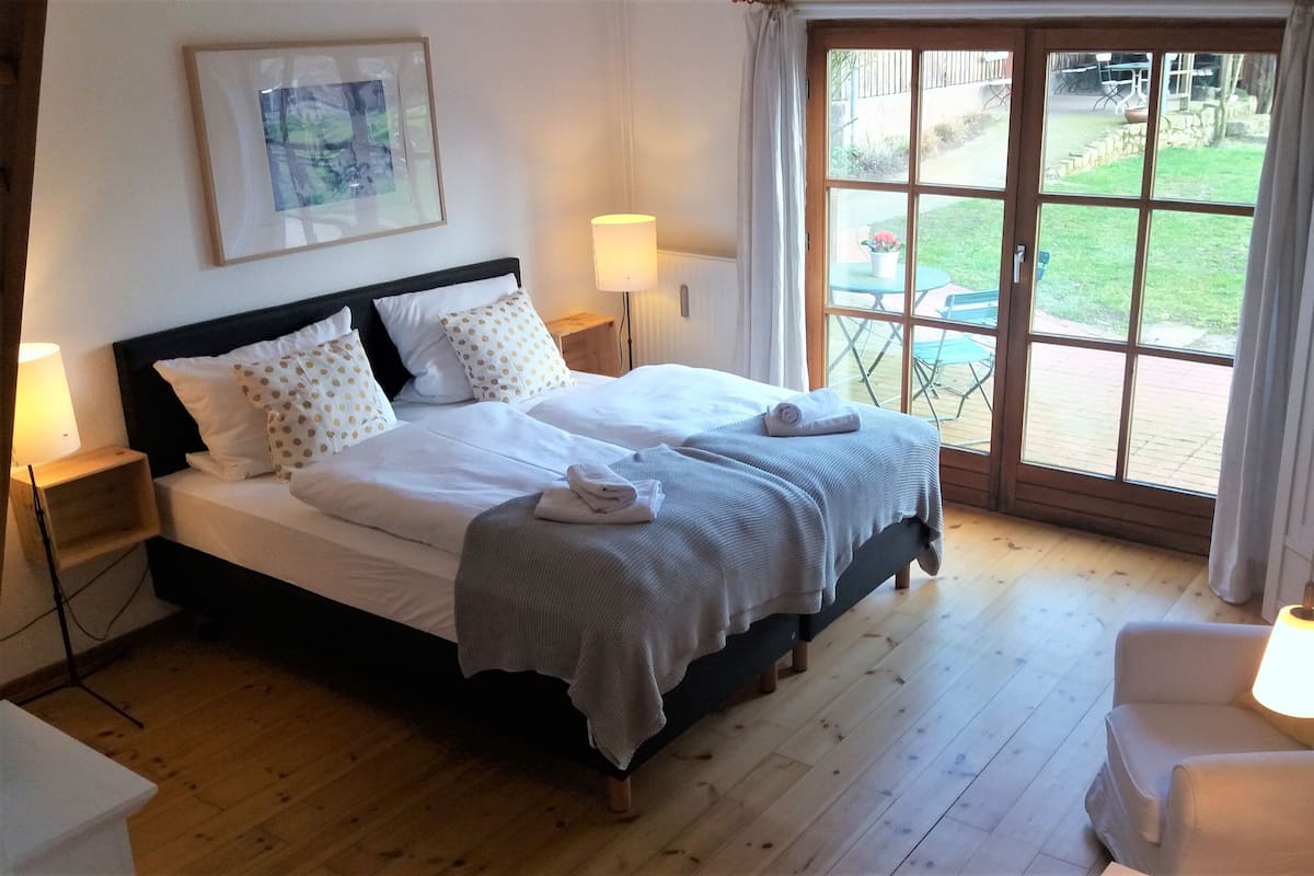 Een slaapkamer met een bed, twee bedlampen, een stoel en uitzicht op de natuur.