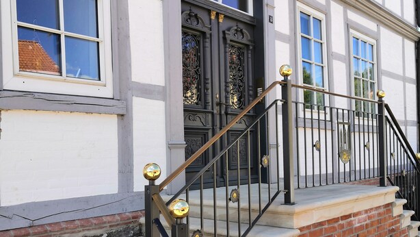 A building with a brick and stone facade, a black metal staircase with gold accents, and a black door with ornate metalwork.