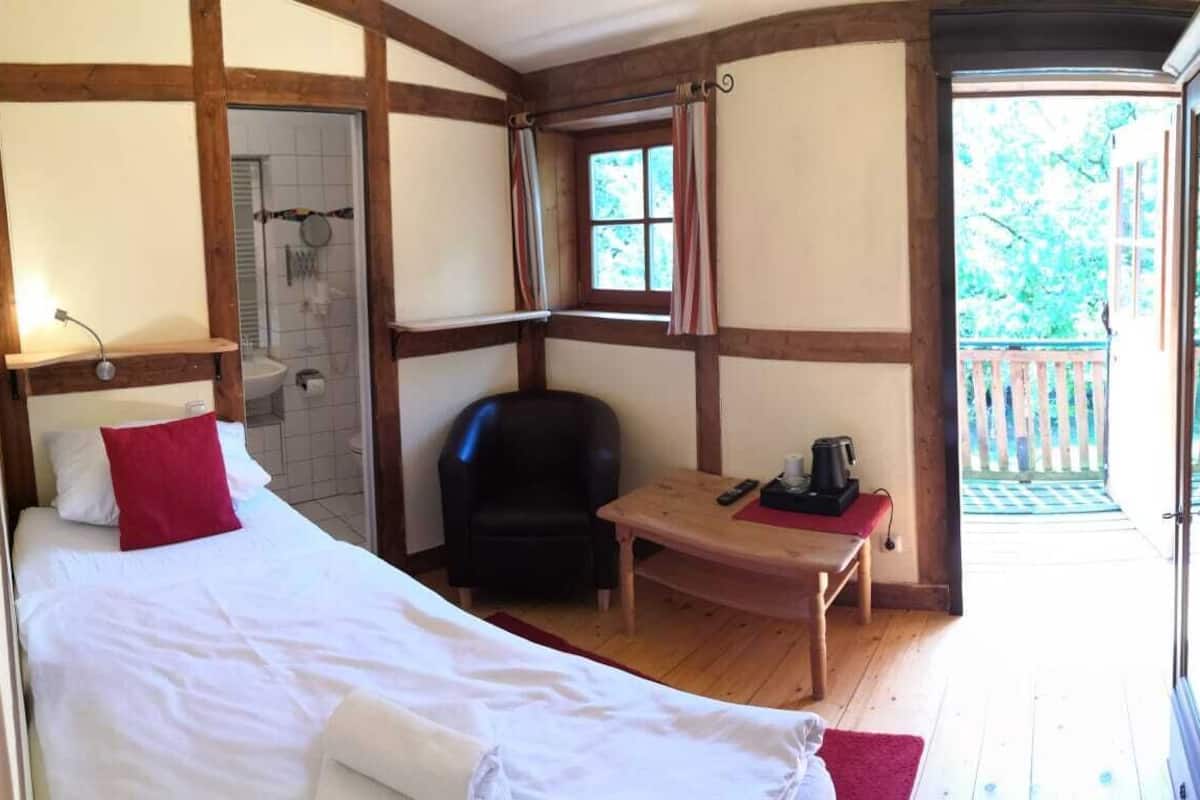 Een slaapkamer met een bed, een stoel, een klein tafeltje, een raam en een deur die uitkomt op een balkon.
