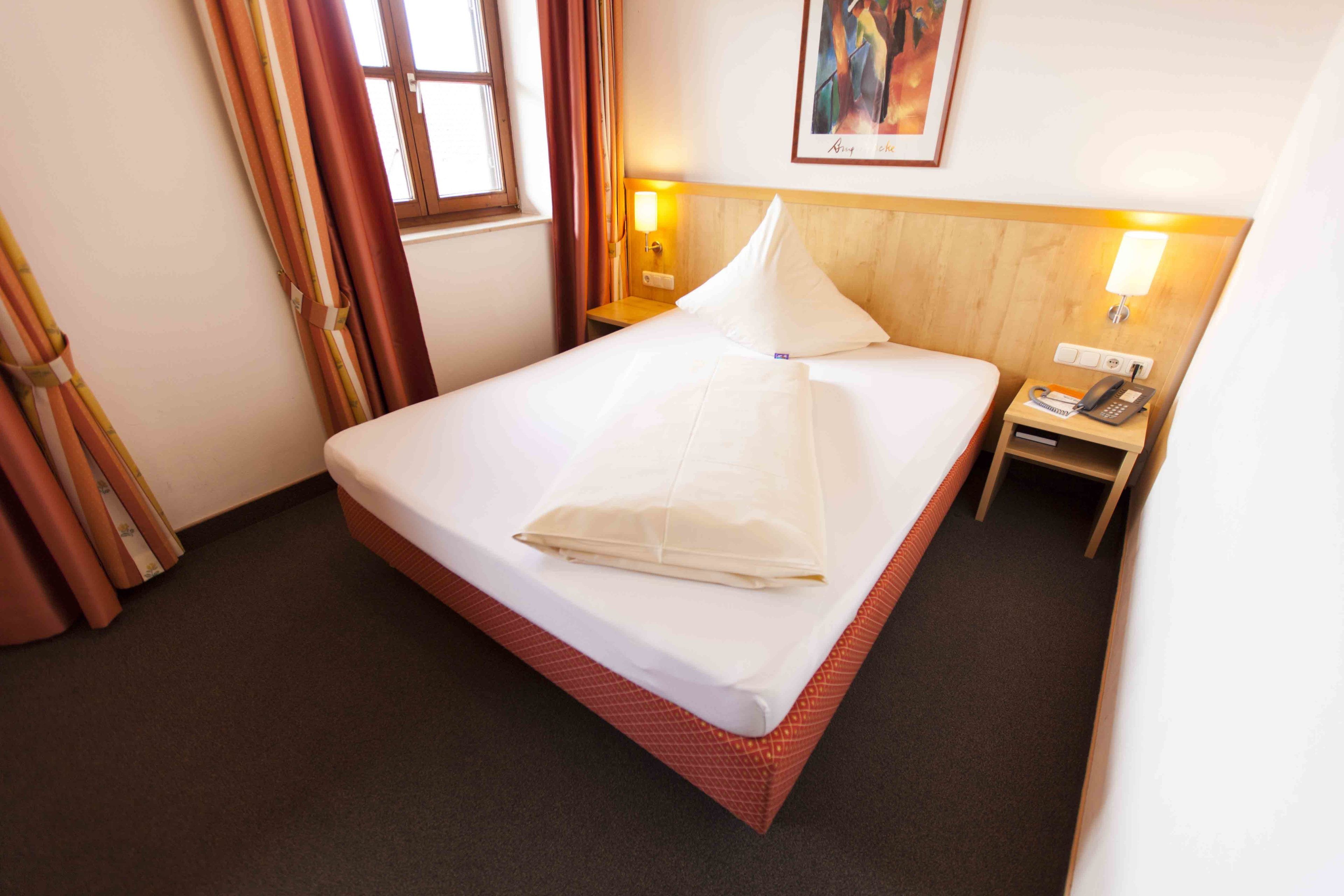 Een hotelkamer met een net opgemaakt bed, een nachtkastje met een telefoon en een schilderij aan de muur.