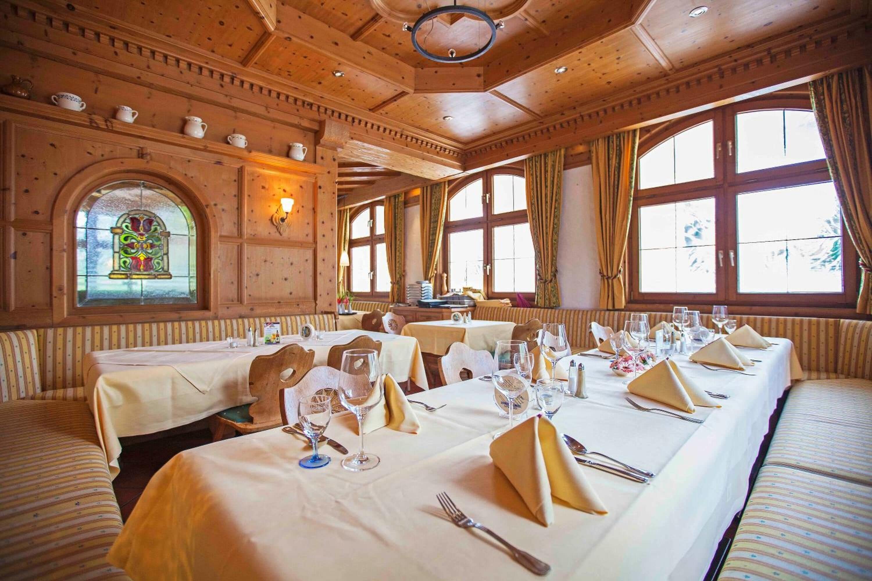 Une salle à manger avec de longues tables dressées pour le repas, des boiseries et de grandes fenêtres.