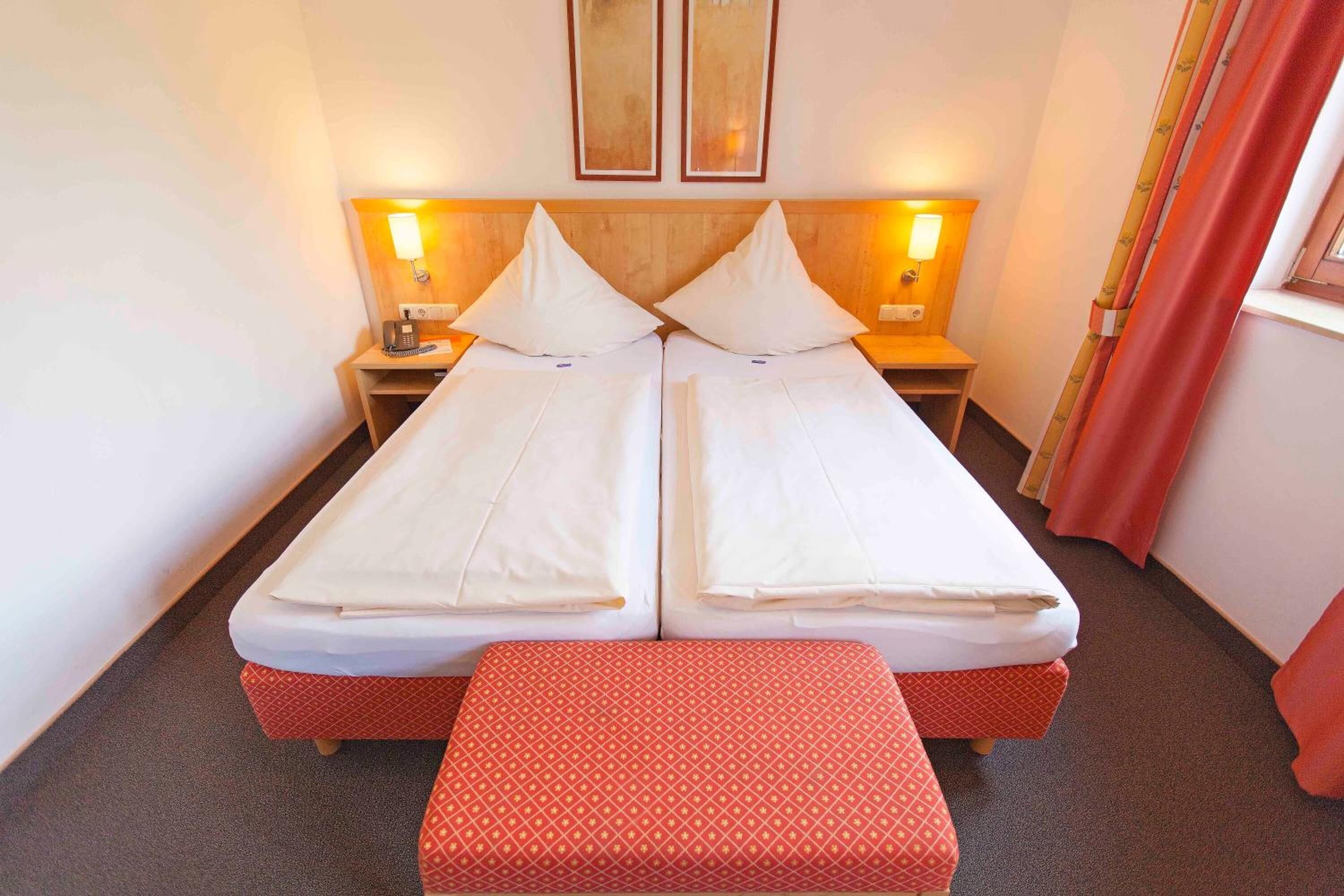 A double bed with two nightstands, a bedside table, and a red bench in a hotel room.