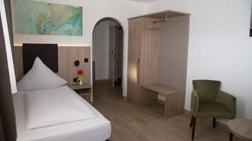 A modern hotel room with a bed, a desk, a chair, and a wardrobe.