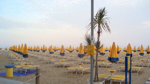A beach with rows of yellow and blue beach umbrellas and lounge chairs. - App'artamento Soyus n.10 (Jesolo)