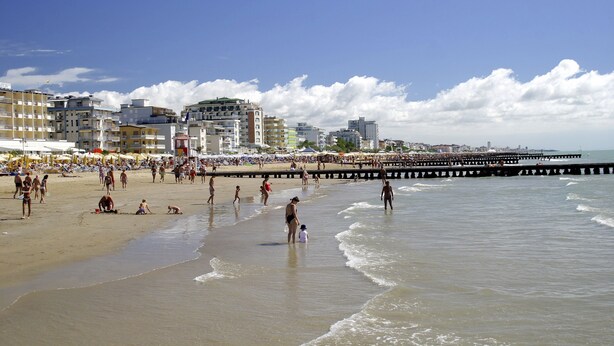A beach with people, a pier, and buildings in the background. - App'artamento Soyus n.10 (Jesolo)