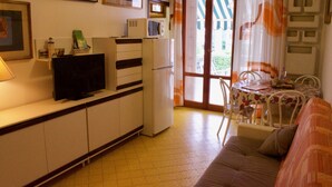 A compact living space with a kitchenette, a sofa, a dining table, and a television. - App'artamento Soyus n.10 (Jesolo)