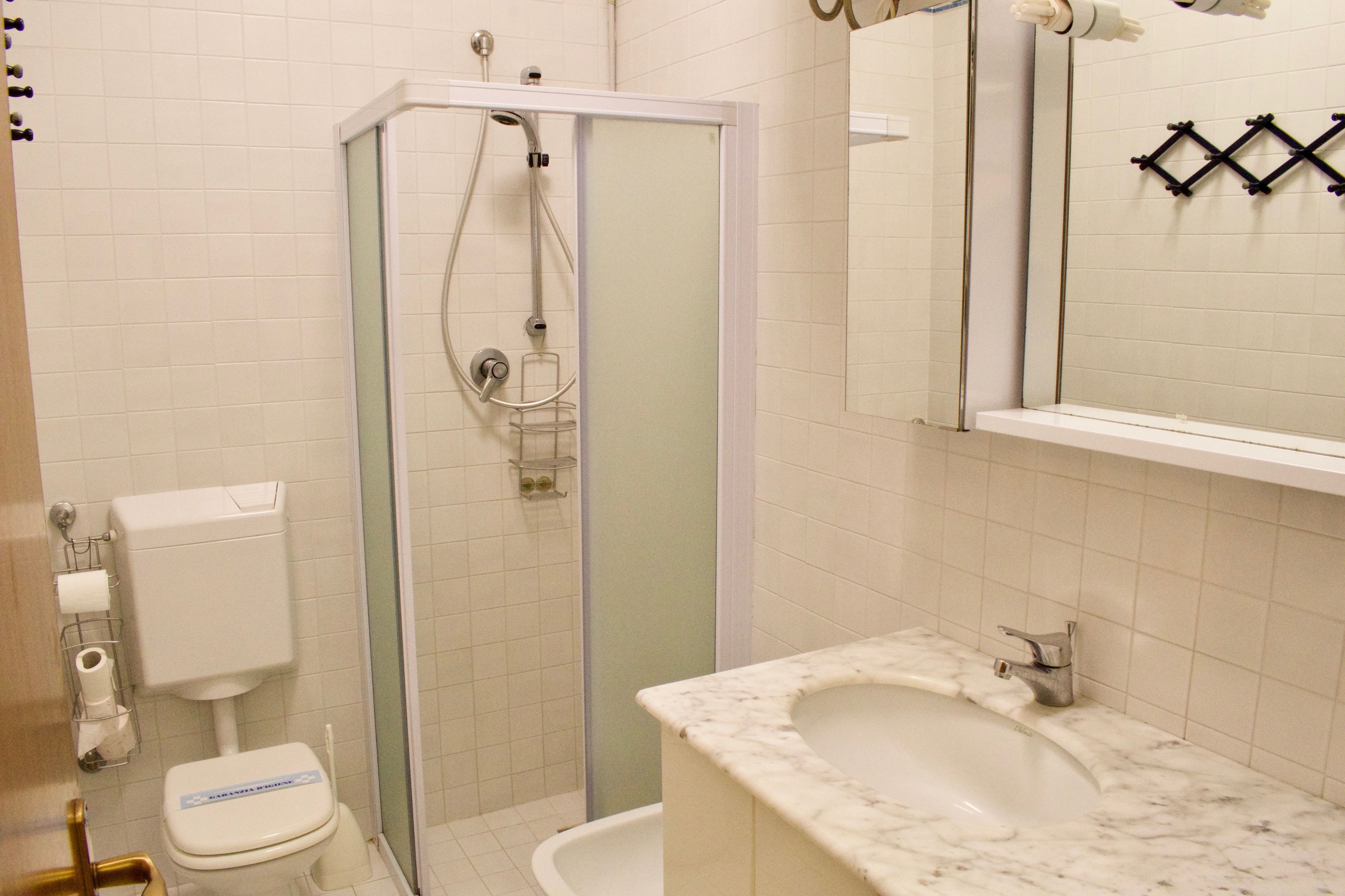 A bathroom with a glass-enclosed shower, a toilet, a sink, and a mirror.
