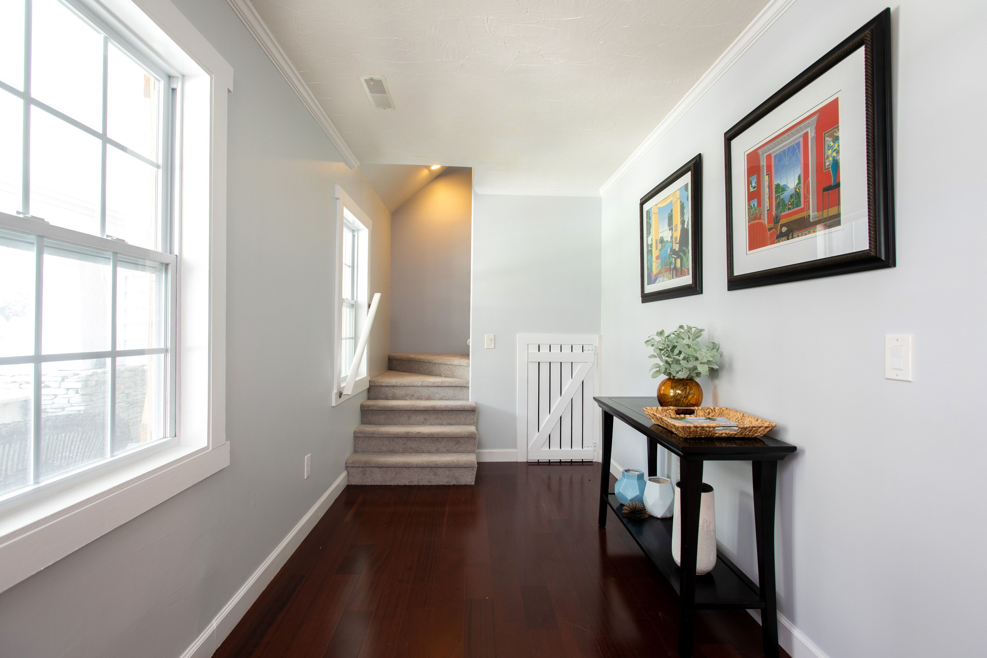A hallway with a wooden floor, a staircase, and a white door at the end.
