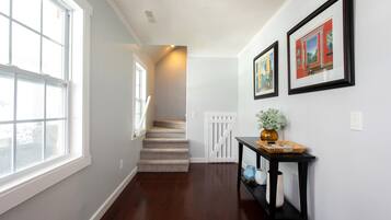 A hallway with a wooden floor, a staircase, and a white door at the end.