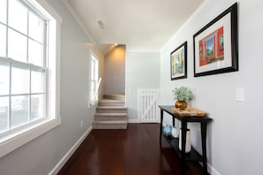 A hallway with a wooden floor, a staircase, and a white door at the end. - WOW! Pool+Pizza Oven near Beaches, Downtown & UNCW (Wilmington)