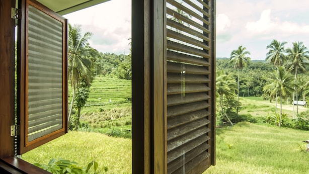 A room with a large window overlooking a lush, green landscape with palm trees and terraced fields. - OYO 882 Puri Gevana Guest House (Padang Panjang)