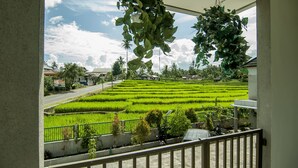 A view from a balcony overlooking a neatly arranged rice field with a clear sky. - OYO 882 Puri Gevana Guest House (Padang Panjang)