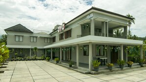 A two-story building with a covered patio area, multiple windows, and potted plants. - OYO 882 Puri Gevana Guest House (Padang Panjang)