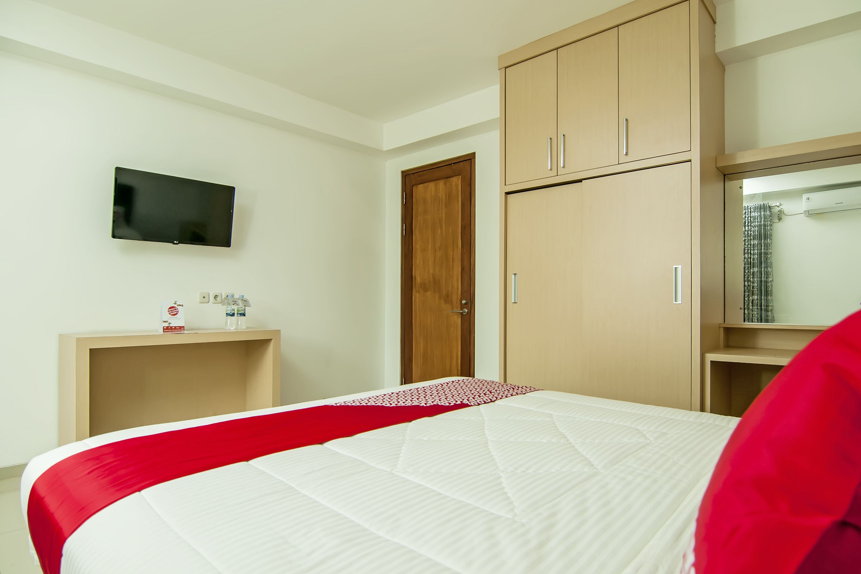 Habitación de hotel con cama, televisor montado en la pared, armario de madera y una mesita con artículos de aseo.