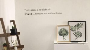 A bedroom with a wooden ladder shelf holding potted plants, a white dresser, and two framed botanical prints on the wall. - Bed and breakfast Style (Rome)