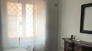 A room with a dining table and chairs, a dark wooden cabinet, a hanging pendant light, and a window with sheer curtains. - Bed and breakfast Style (Rome)