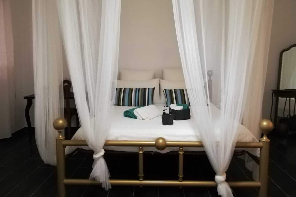 A four-poster bed with white curtains, a gold frame, and striped pillows.