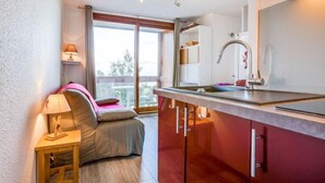 Una cocina compacta con lavamanos integrado, un pequeño comedor con mesa y sillas, y un sofá con lámpara.