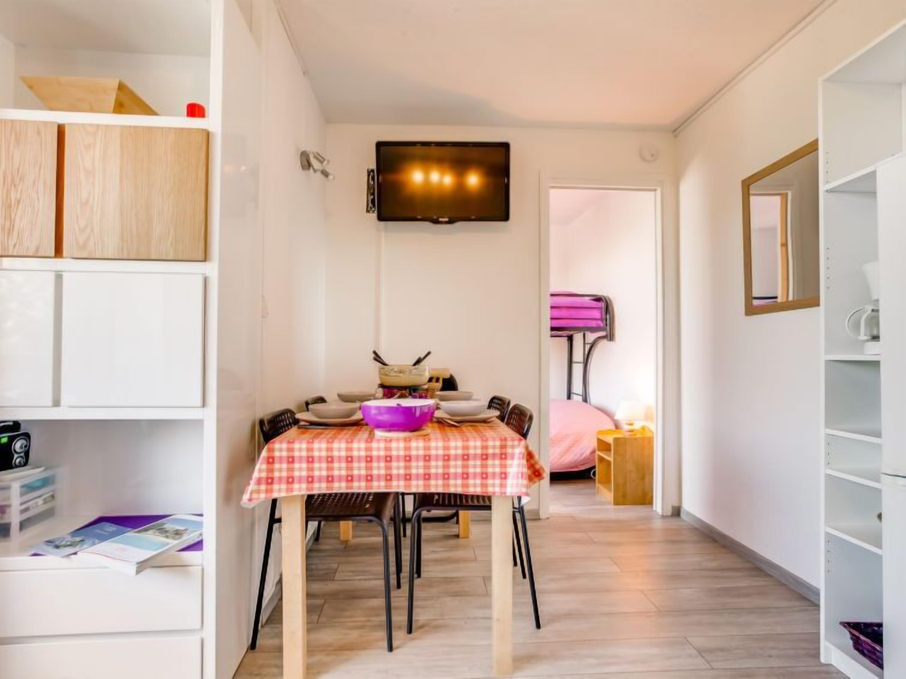 A compact living space with a dining area, a television mounted on the wall, and a kitchenette area.