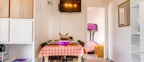 A compact living space with a dining area, a television mounted on the wall, and a kitchenette area.