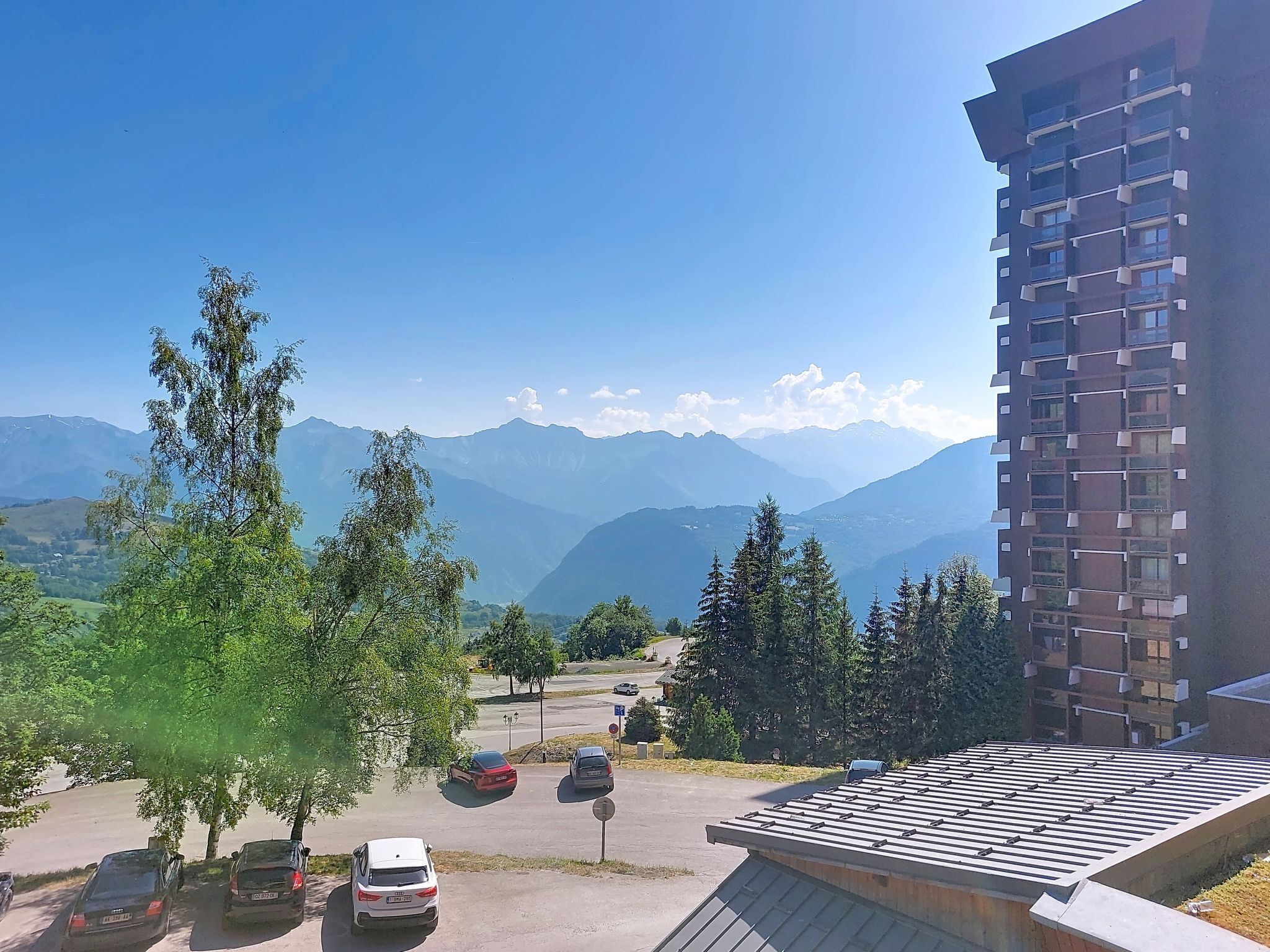 Un parking avec des voitures, des arbres et une chaîne de montagnes en arrière-plan.