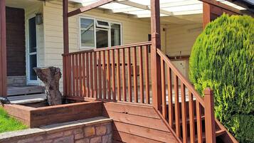 A wooden deck with a stone wall, a wooden staircase, and a green bush.