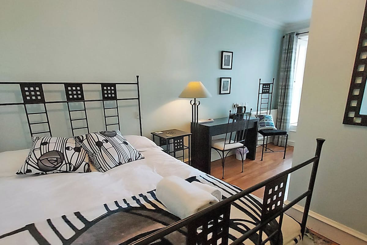 A bedroom with a bed, a desk, and a chair. There are two pillows on the bed.