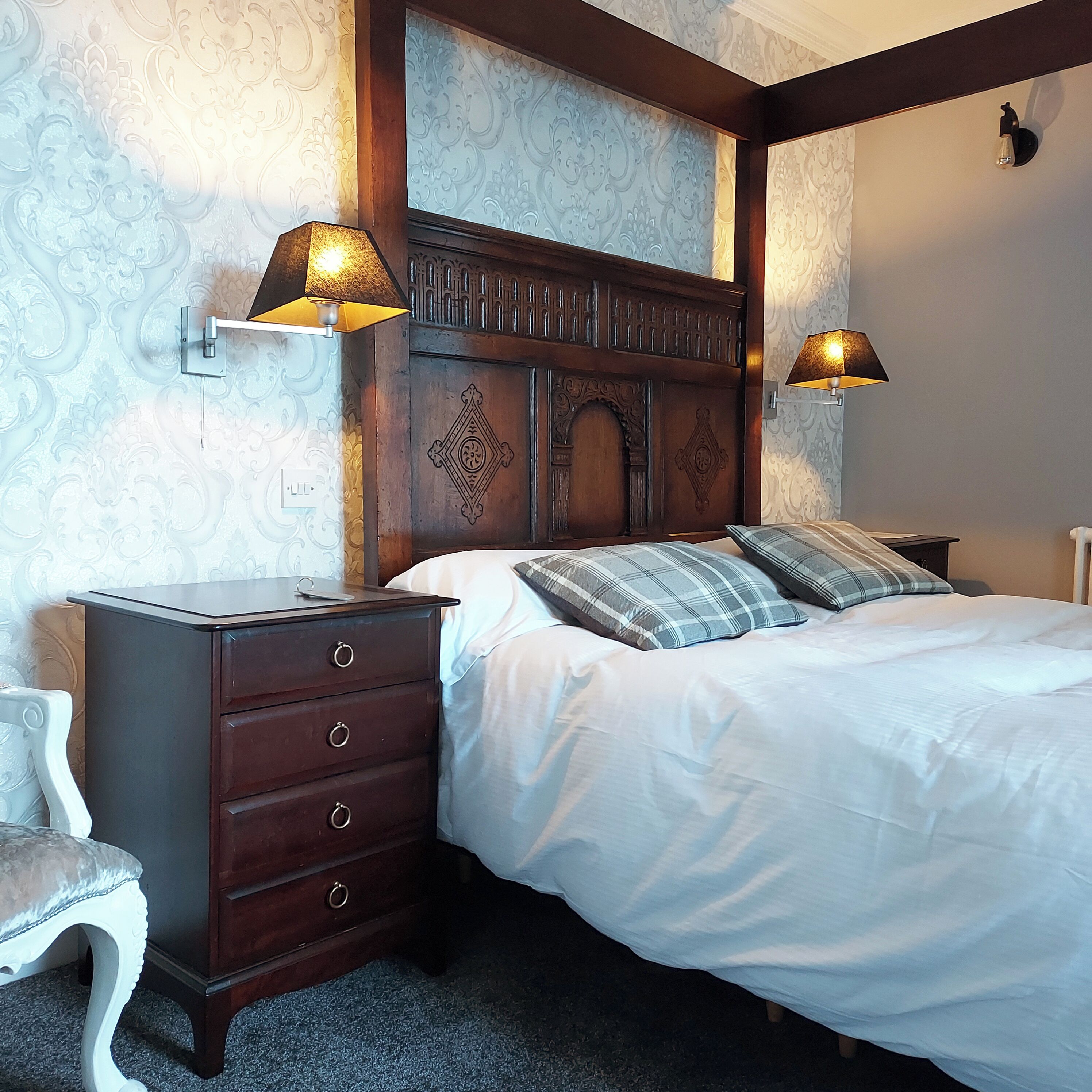 Une chambre à coucher avec une tête de lit en bois, un lit avec une literie blanche, deux lampes de chevet et une table de chevet avec des tiroirs.