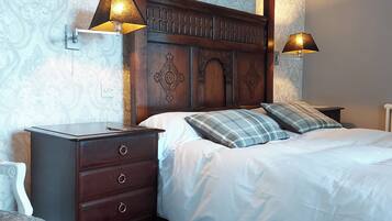 Une chambre à coucher avec une tête de lit en bois, un lit avec une literie blanche, deux lampes de chevet et une table de chevet avec des tiroirs.