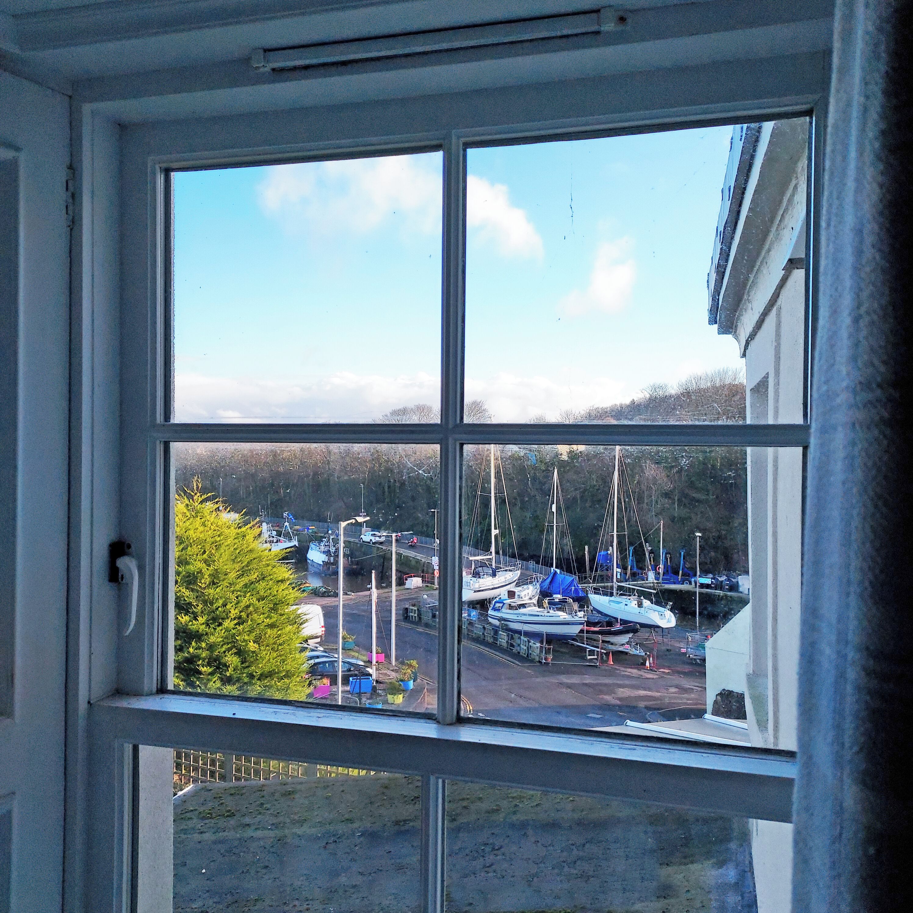 A view through a window of a marina with boats docked, a road, and a building in the background.