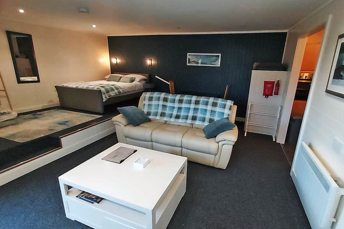 A compact hotel room with a bed, a sofa, a coffee table, and a small cabinet.
