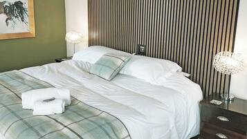 A neatly made bed with white linens, a plaid blanket, and a folded towel. There are two bedside lamps and a wall-mounted light fixture.