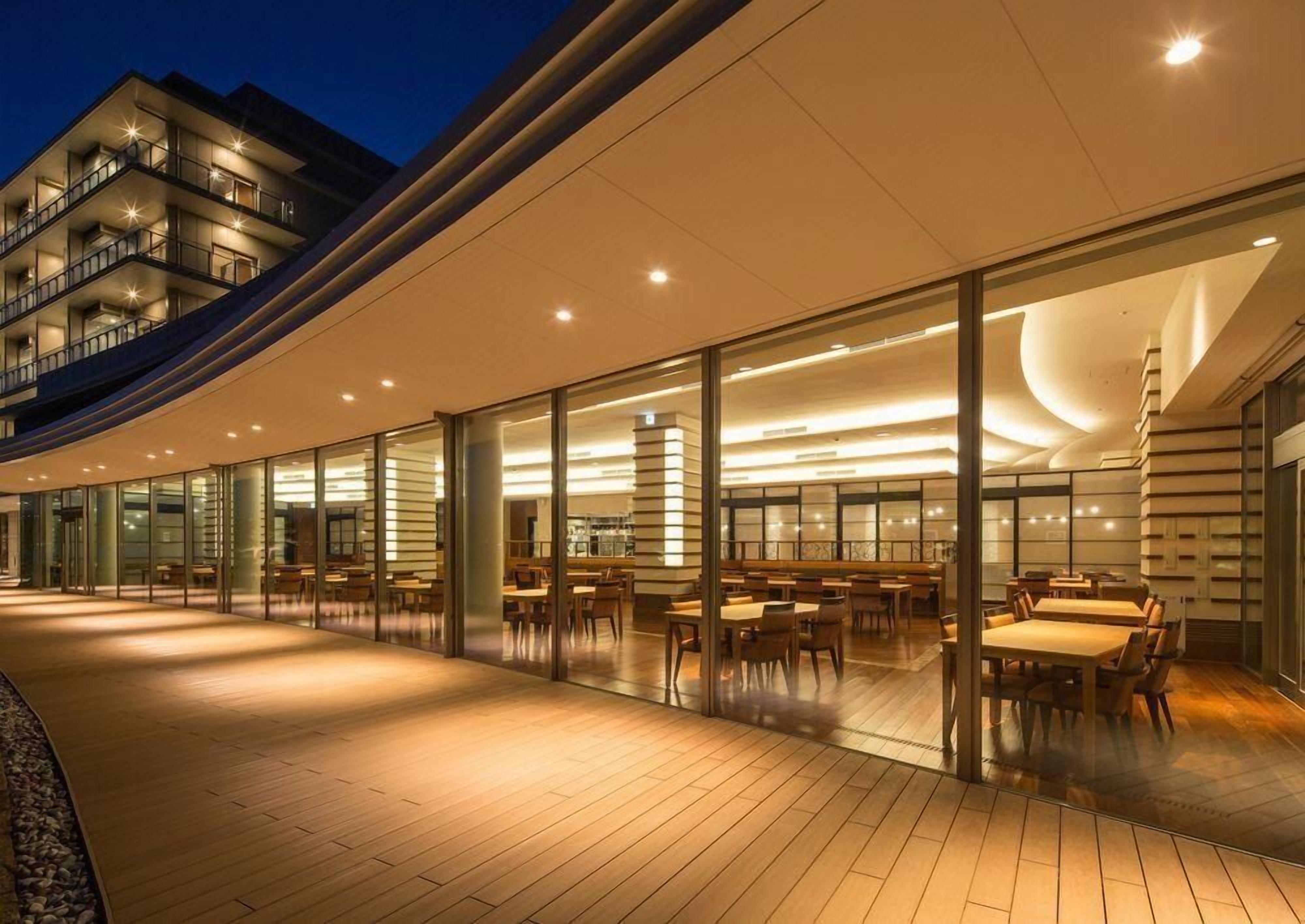 Un hôtel moderne avec une façade en verre, un espace extérieur aménagé pour s’asseoir et une structure de toit incurvée.