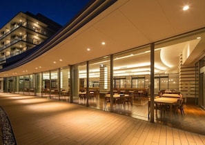 Un hôtel moderne avec une façade en verre, un espace extérieur aménagé pour s’asseoir et une structure de toit incurvée.