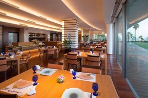 A modern restaurant with tables set for dining, a bar area, and large windows offering a view. - Hotel Kaze no Umi (Shimonoseki)