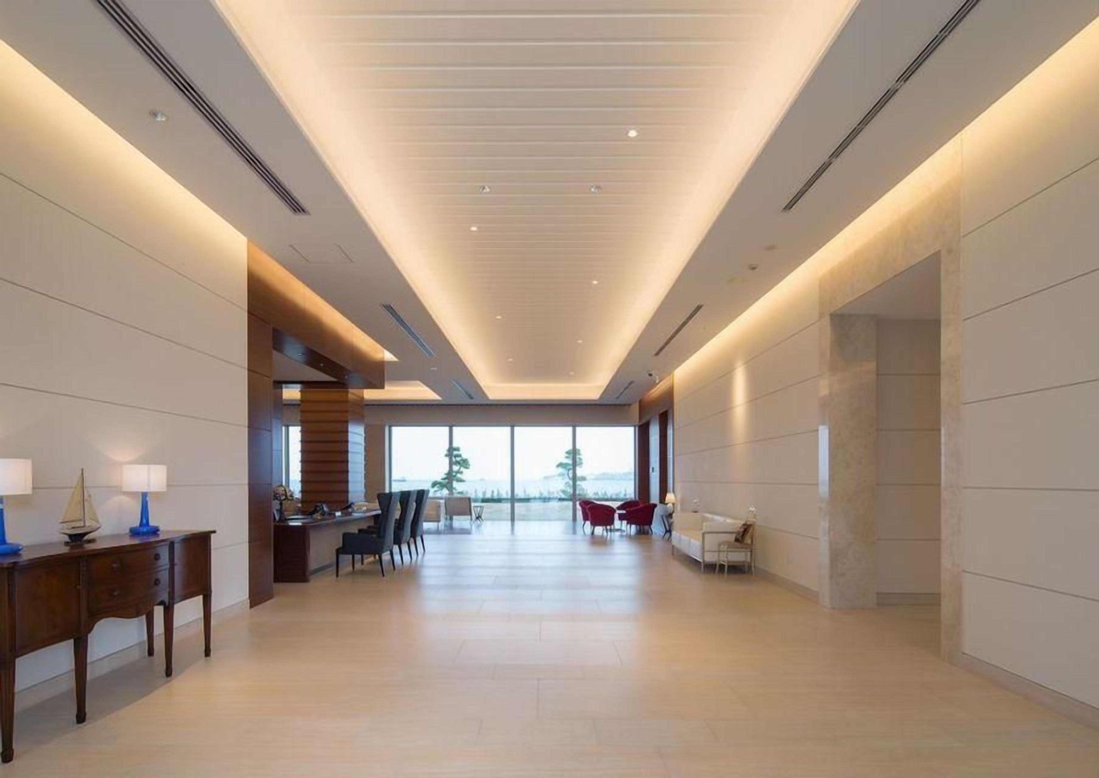 A spacious hotel lobby with a high ceiling, a reception desk, seating area, and large windows offering a view.