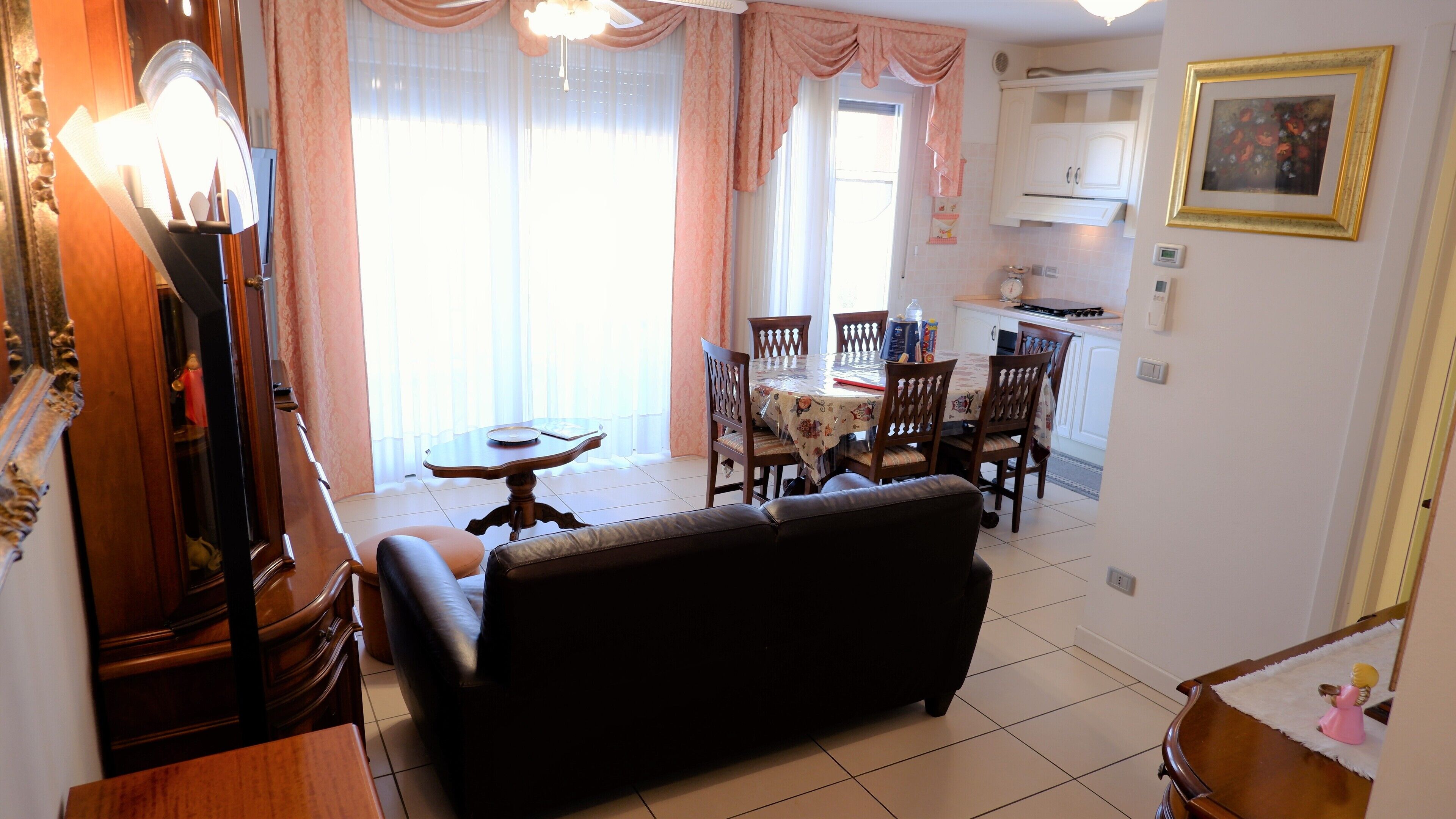 Un salon avec un canapé, une table à manger avec des chaises, un coin cuisine et une grande fenêtre avec des rideaux.