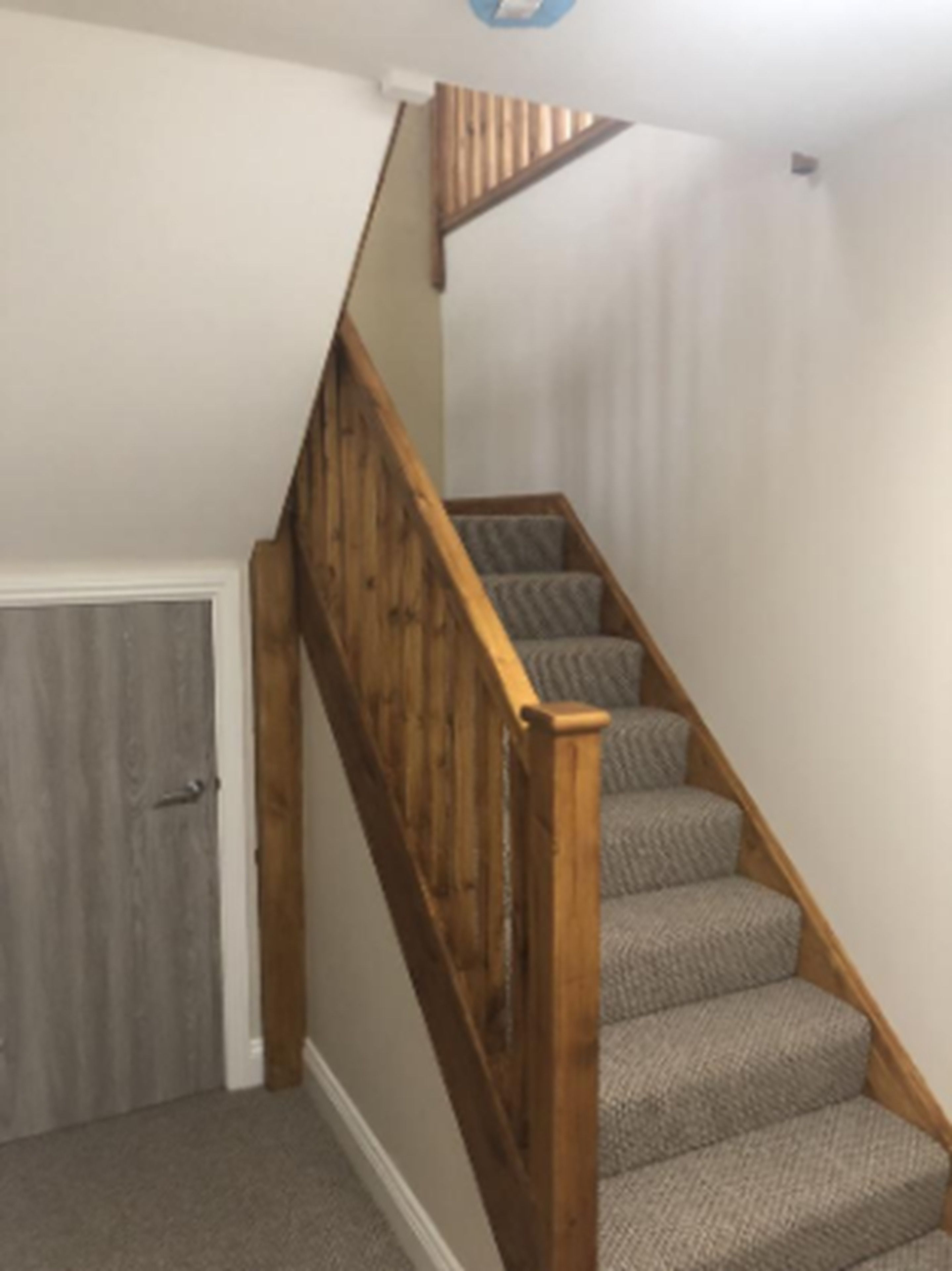 A staircase with wooden railings and grey carpeted steps.