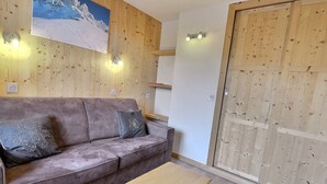 Una habitación con un muro revestido de paneles de madera, un sofá marrón con cojines decorativos, una mesa de madera y una puerta de madera.