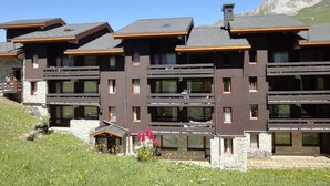 Un hotel de varios pisos con balcones, detalles de piedra y montañas al fondo.