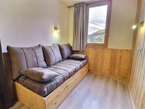 A wooden sofa bed in a room with a window, wooden walls, and a light switch.