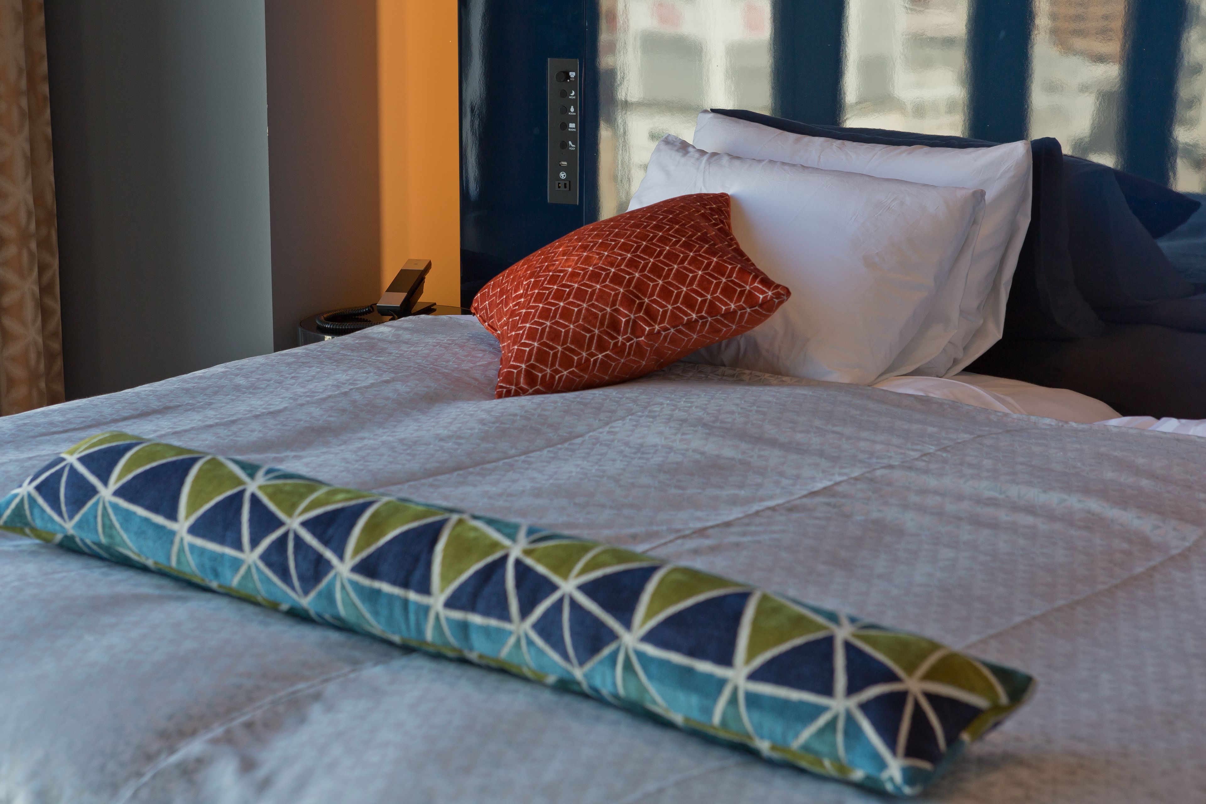 A neatly made bed with a patterned pillow, a plain pillow, and a blanket.