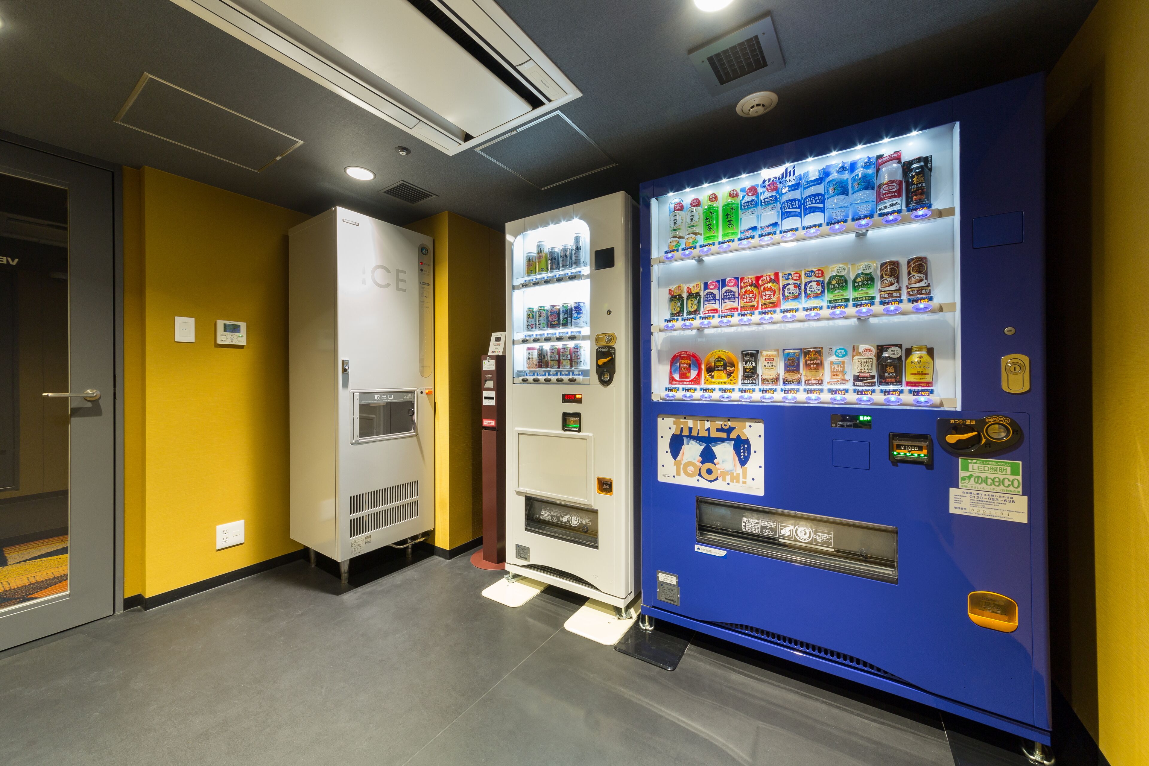 Máquina de vendas com diversas bebidas e lanches, uma geladeira e uma porta com puxador.
